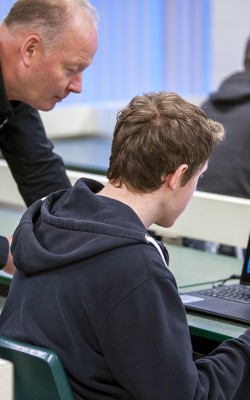 Teacher helping student with coding on computer