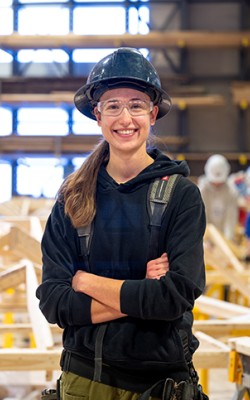 A female carpenter stands in a construction shop.
