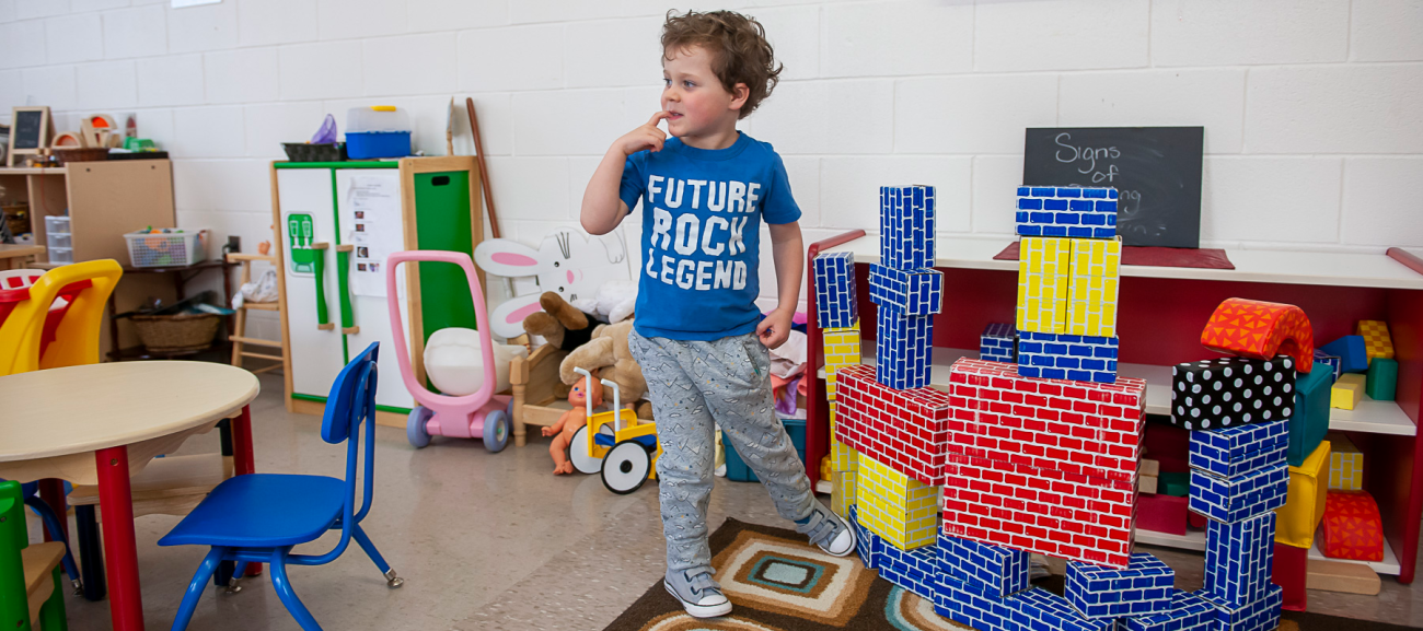Toddler stands in a classroom next to a build with cardboard bricks.