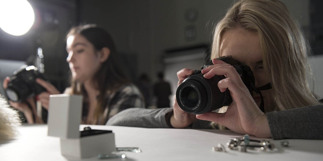 At Fanshawe College's London Campus, two people are photographing jewelry on a white table as part of the Pre-Media program.