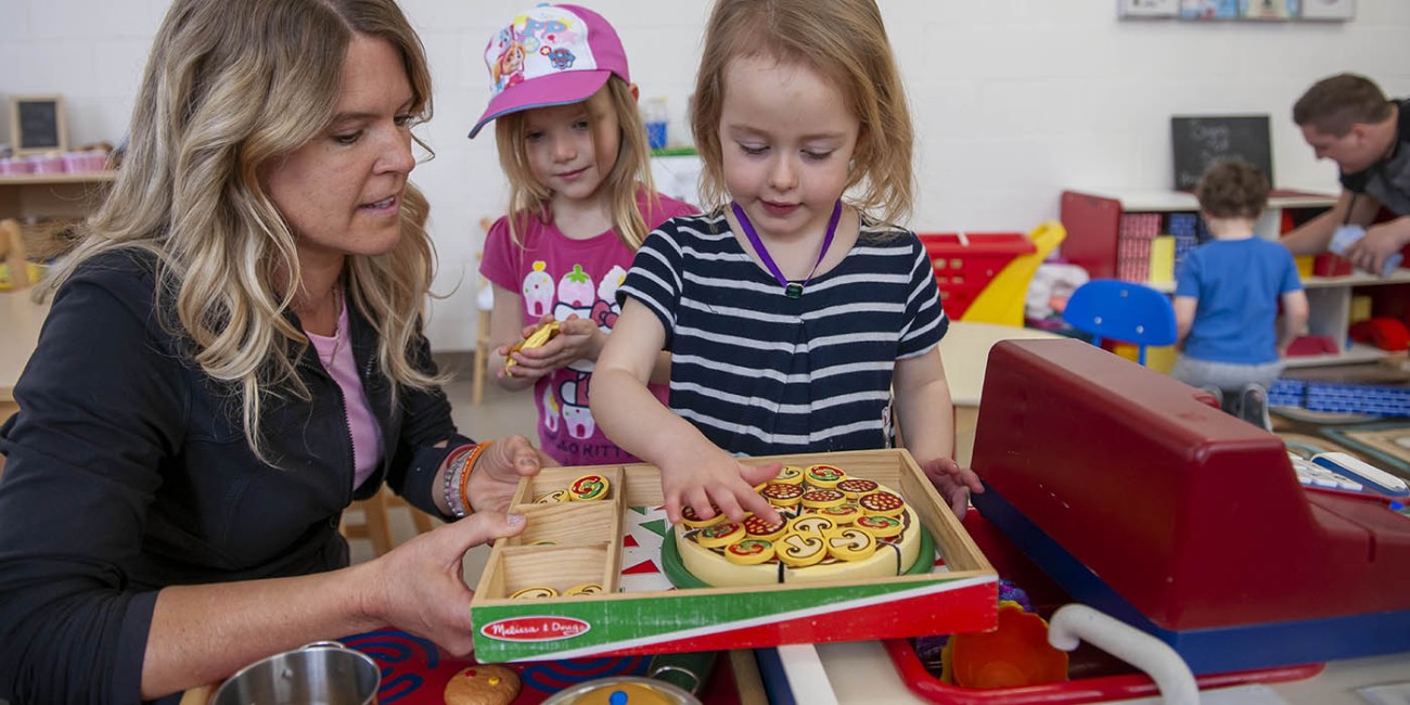 At the Simcoe/Norfolk Regional Campus, Early Childhood Education program participants are outside, playing with rocks on a log.