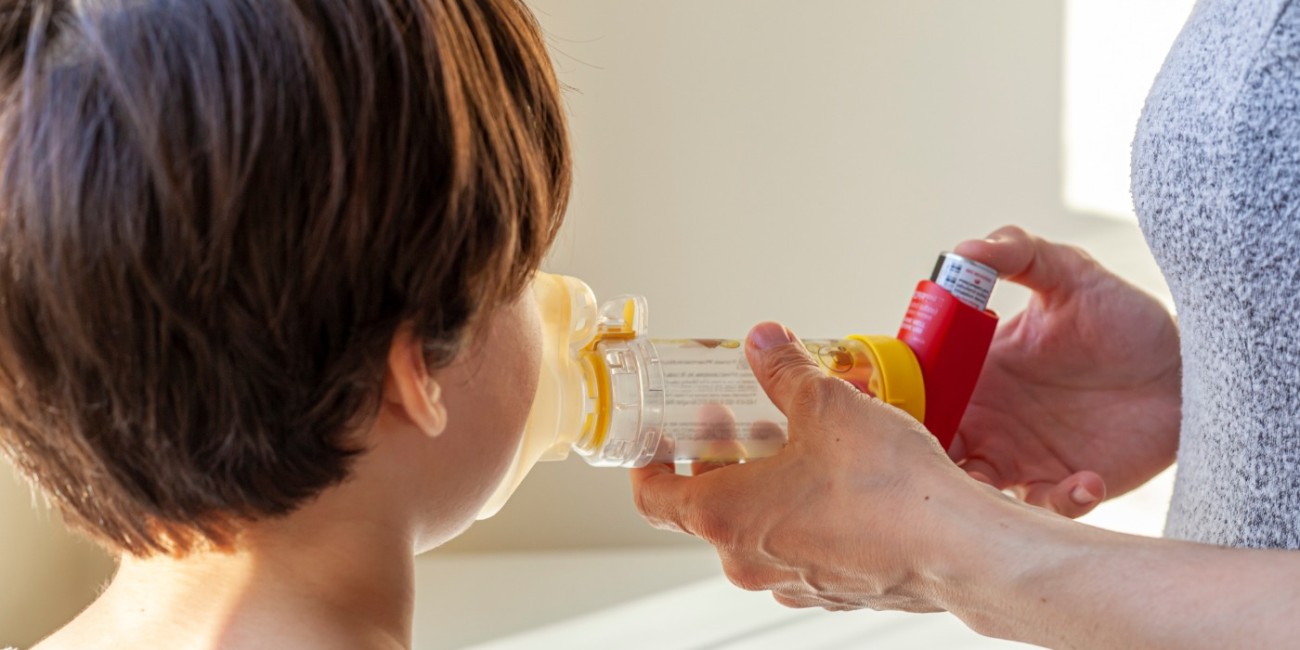 A parent administers an inhaler to a child using a MDI spacer to assist with the absorption of the medication