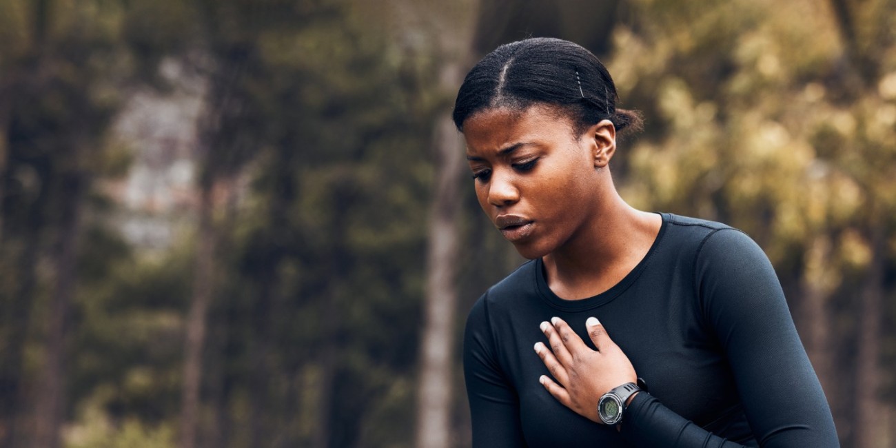 A woman on a run outdoors appears to notice triggers affecting her breathing and stops to catch her breath