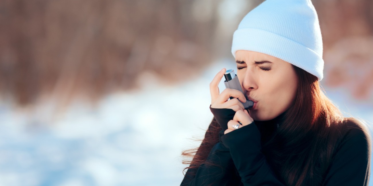 A woman struggling to breathe outdoor in the cold winter air uses an inhaler to support her breathing