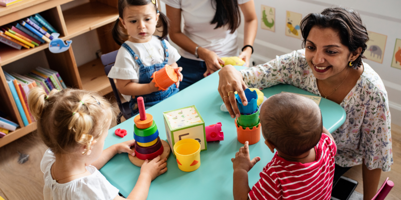 A group of young children play around an aqua coloured table with stacking toys. 
