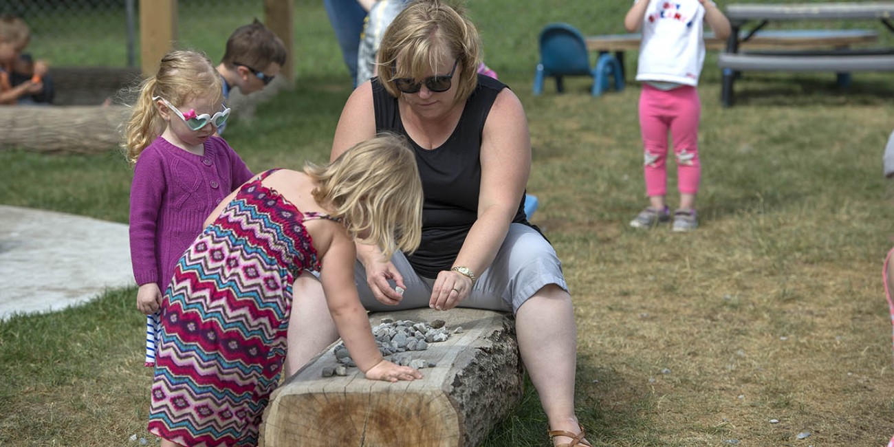 At the Simcoe/Norfolk Regional Campus, Early Childhood Education program participants are outside, playing with rocks on a log.
