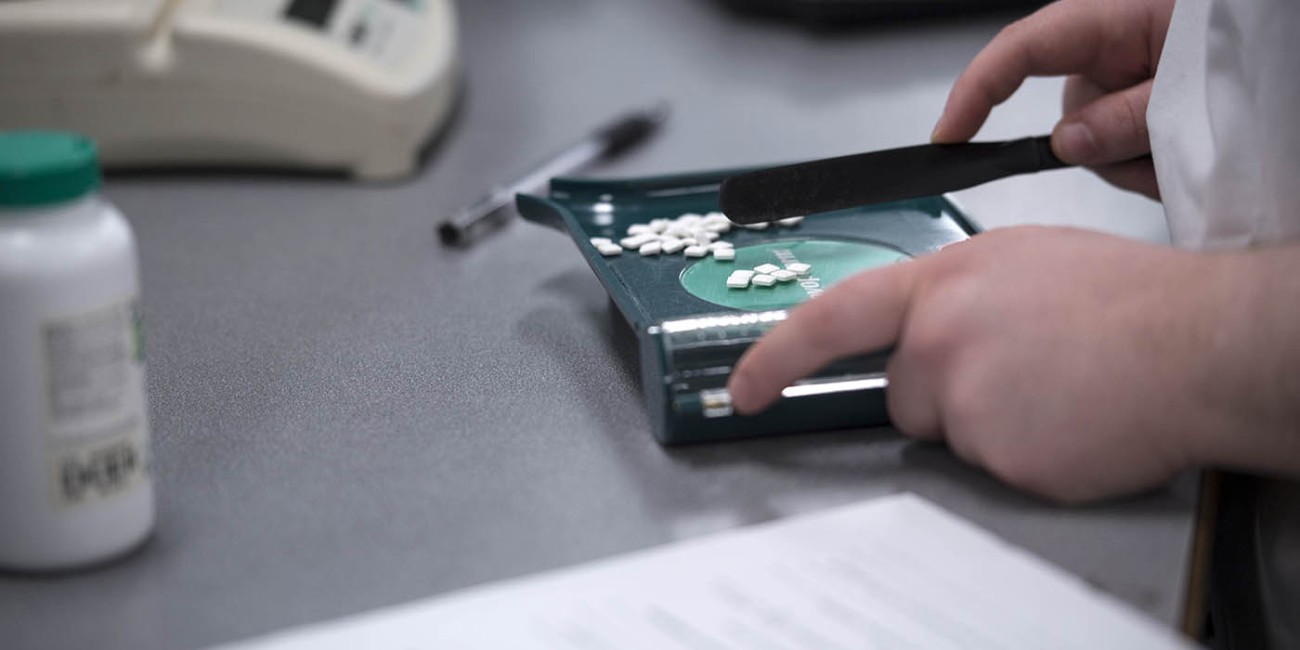 A pharmacy tech sorts medication on a table with a pill sorter