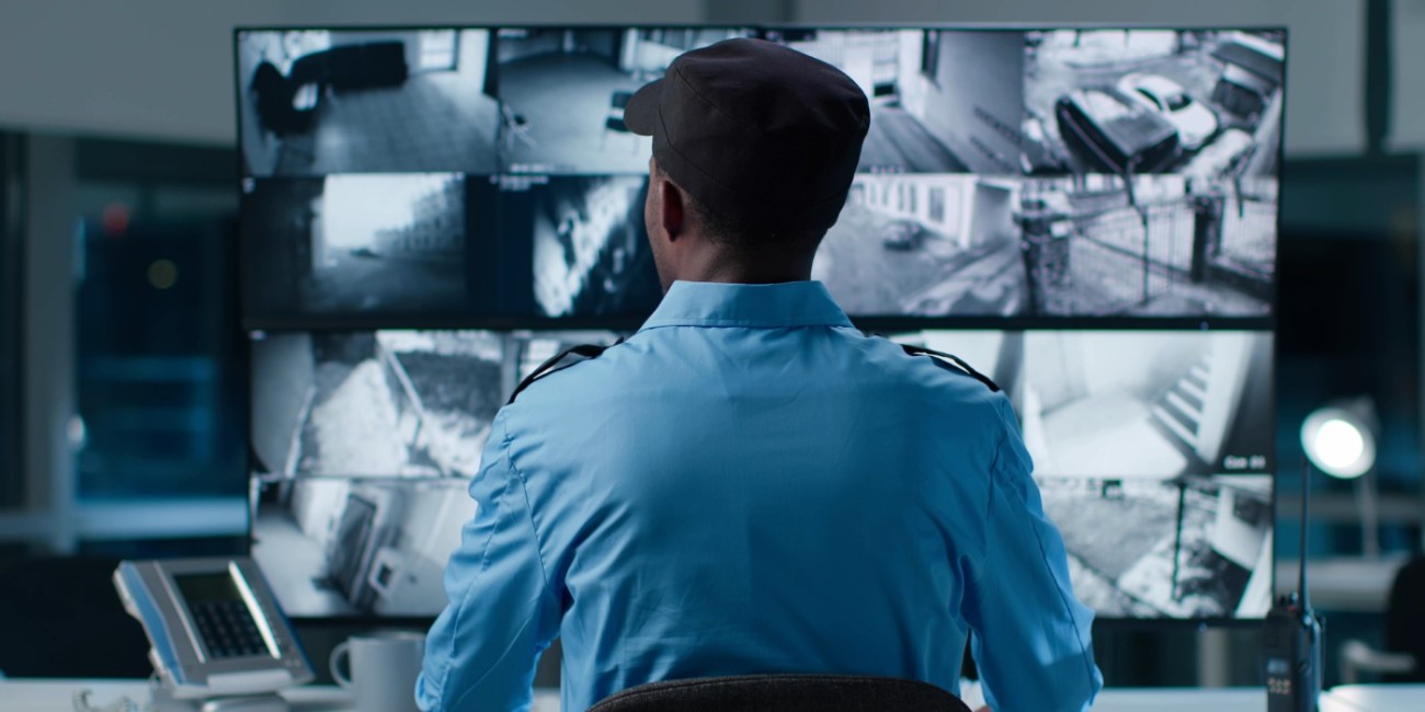 A security professional sits at a bank of security screens scanning for any abnormlities. 