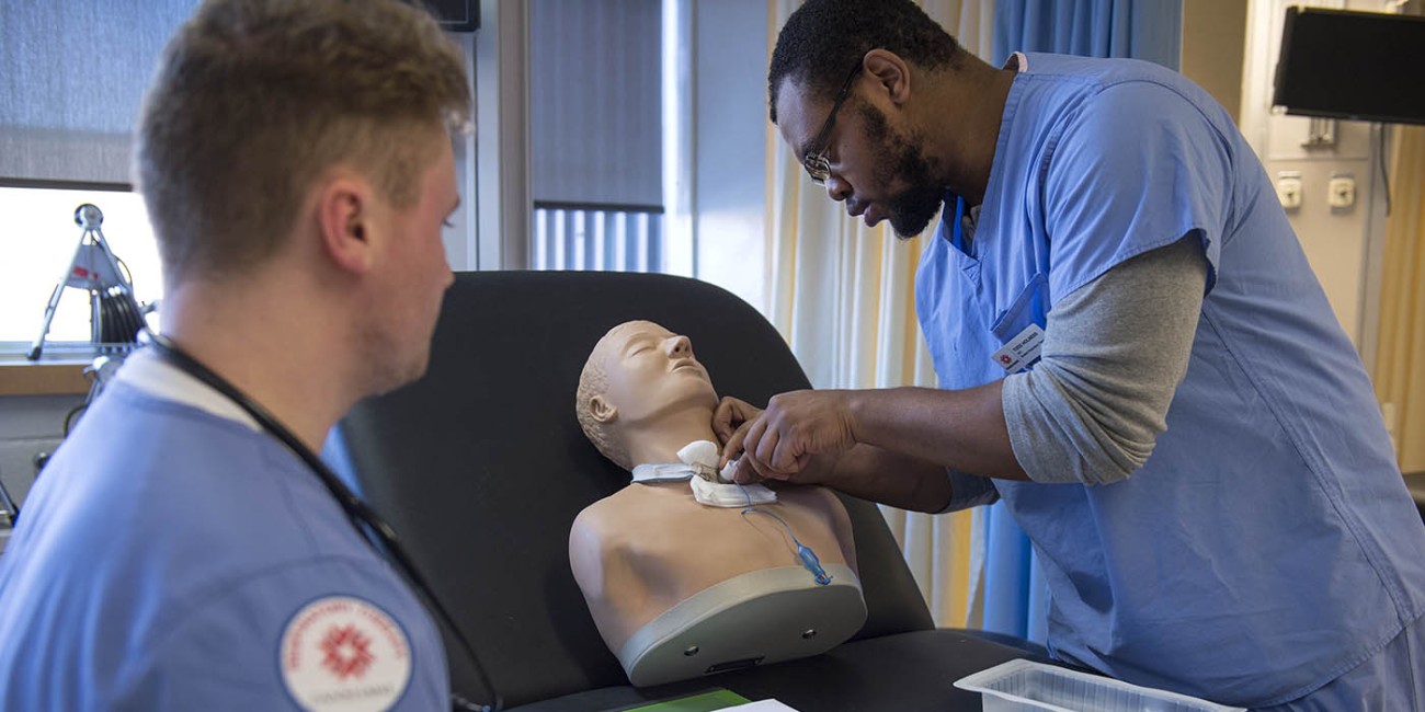 In the School of Health Sciences at Fanshawe College's London Campus, three people in scrubs are gathered around a medical mannequin, practicing a procedure on its neck.