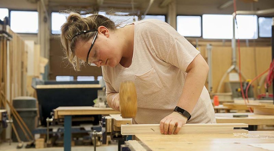 Female student working in carpentry shop with woodworking equipment