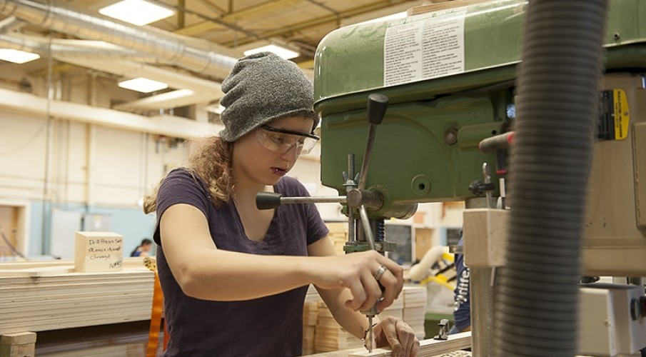 Female student working in carpentry shop with woodworking equipment