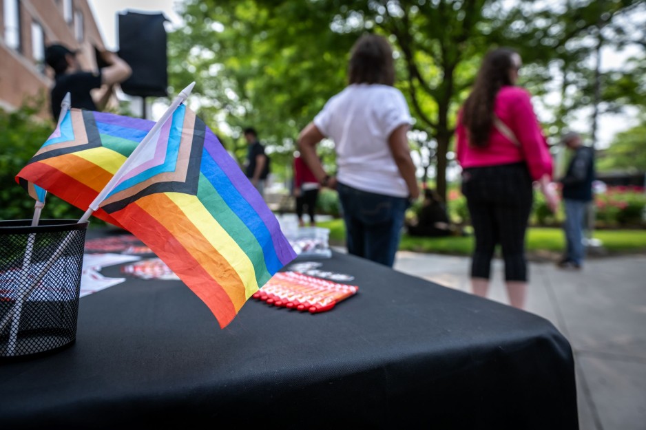 Two small Progress Pride flags on a table in the foreground with people in the background