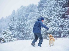 Man with dog plays in snowy forest in winter