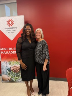 Two women stand next to each other in front of a red and white pop-up banner.