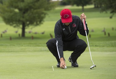 Person with golf club, on golf course, bending over to place ball on green