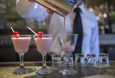 Student working in mixology class, pouring three glasses of pink cocktail