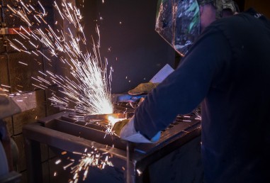 Welding student in dark setting with helmet on and sparks flying