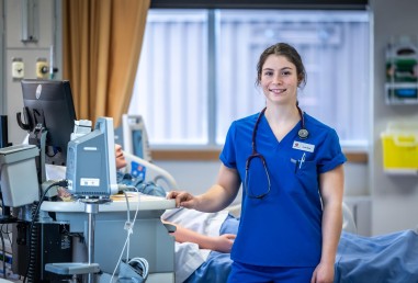 Photo of a nursing student in blue scrubs wearing a stethoscope posing for the camera while wearing at