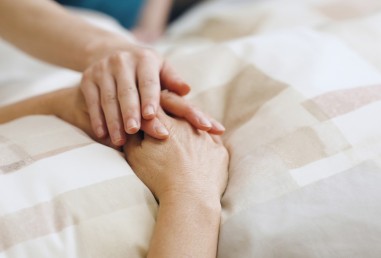 A comforting hand rests gently on another's, conveying empathy and support. The hands lie on a patterned beige blanket, suggesting a serene atmosphere.