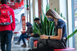 Girl sitting in a hallway looking at her phone, as a student with a red backpack walks by