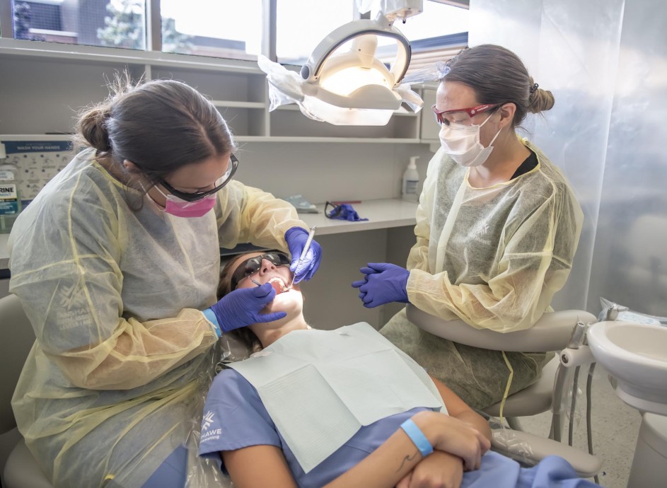 Two people working on a dental patient in the dental assisting lab