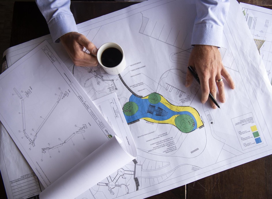 Honours Bachelor of Environmental Design and Planning student's playground plans on table with coffee cup in one hand