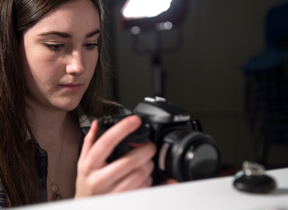 Girl with camera taking photo of small object in studio