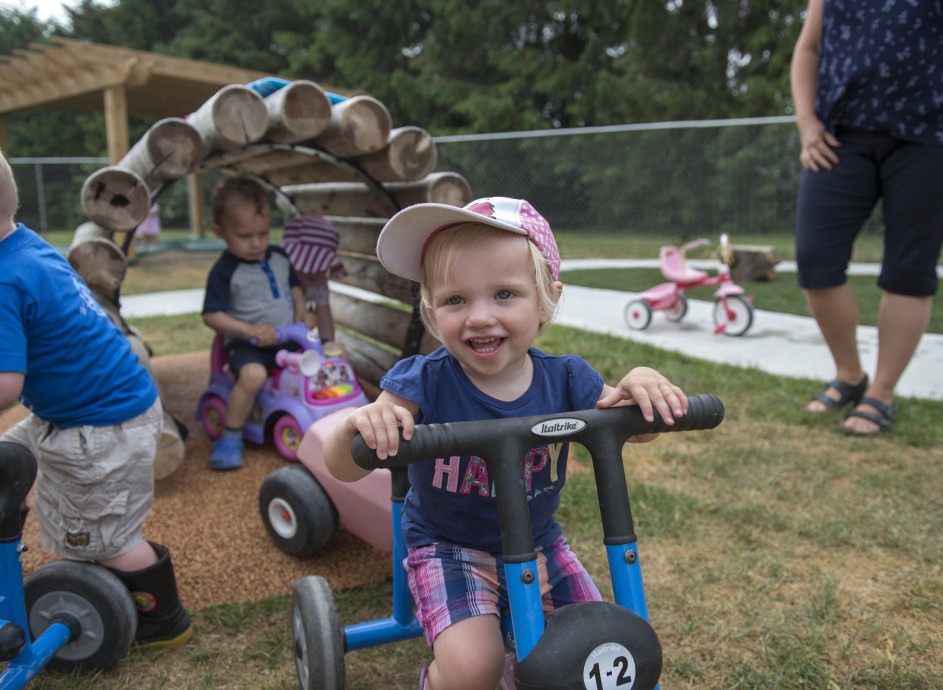 Children laughing and playing outside on tricycles while an caregiver looks on