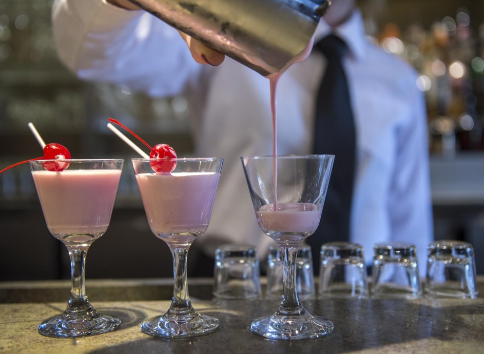 Student working in mixology class, pouring three glasses of pink cocktail