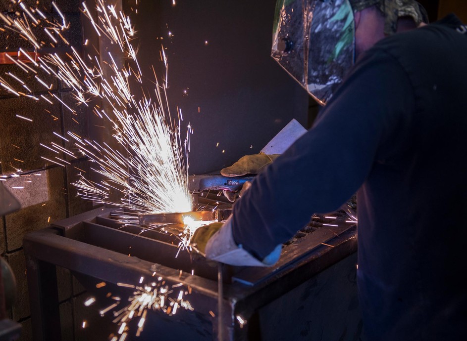 Welding student in dark setting with helmet on and sparks flying