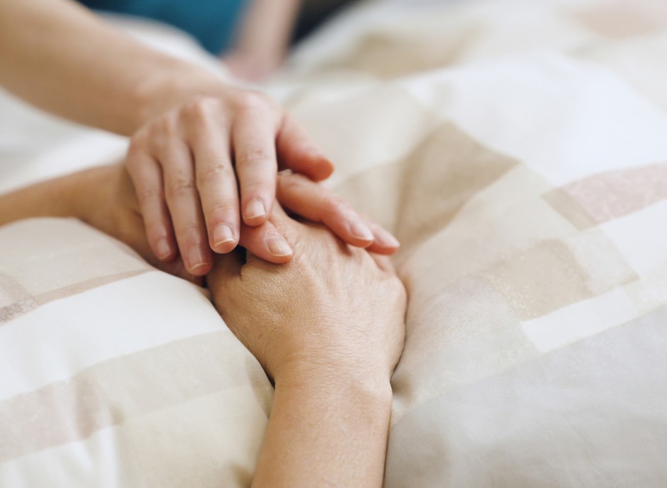 A comforting hand rests gently on another's, conveying empathy and support. The hands lie on a patterned beige blanket, suggesting a serene atmosphere.