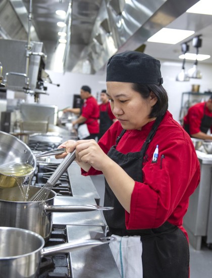 Culinary student pouring liquid into pot on stove in culinary lab