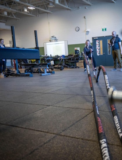 At the Fanshawe College London Campus, a person is using battle ropes in the Fitness and Health Promotion program's gym, while another person observes.