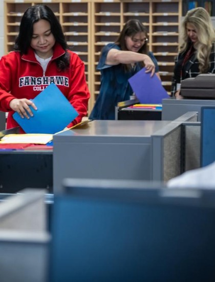In a classroom at Fanshawe College's London Campus, individuals are working with files and computers in an office administration setting.
