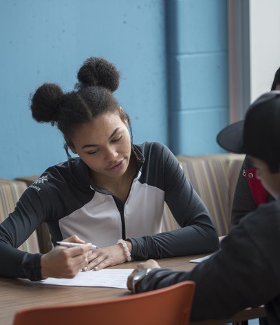 Three students sitting at table talking and filling out form