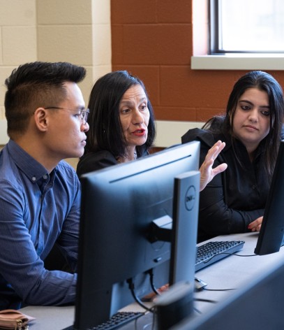two students listening to instructor in front of a computer