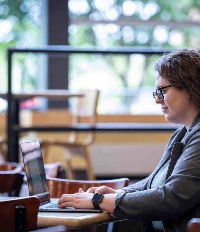 student sits in cafe working on laptop