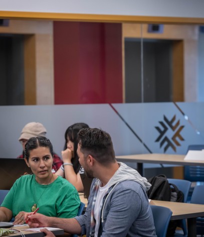 Two people sit at a table, one in a green shirt and the other in a grey hoodie, engaged in conversation.