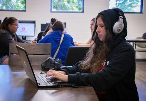 Photo of a student working on their laptop with headphones one