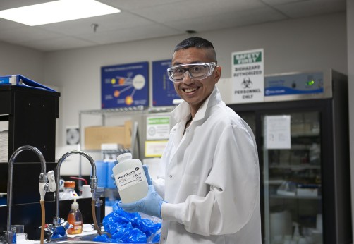 alum smiles while holding a bottle in a lab