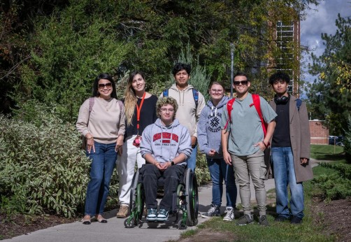 A group poses on a pathway at Fanshawe College's London Campus, with lush greenery and a brick building in the background.