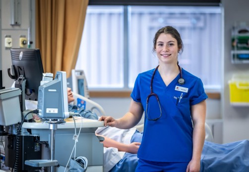 Photo of a nursing student in blue scrubs wearing a stethoscope posing for the camera while wearing at