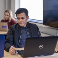 Student working on laptop in busy classroom