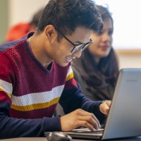 Smiling student working on laptop in busy classroom