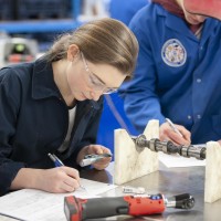 Automotive Service Technician student writing at a table in an automotive lab