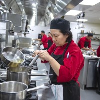 Culinary student pouring liquid into pot on stove in culinary lab