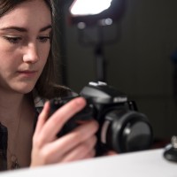 Girl with camera taking photo of small object in studio