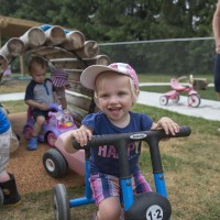 Children laughing and playing outside on tricycles while an caregiver looks on