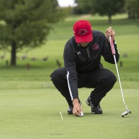 Person with golf club, on golf course, bending over to place ball on green