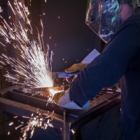 Welding student in dark setting with helmet on and sparks flying
